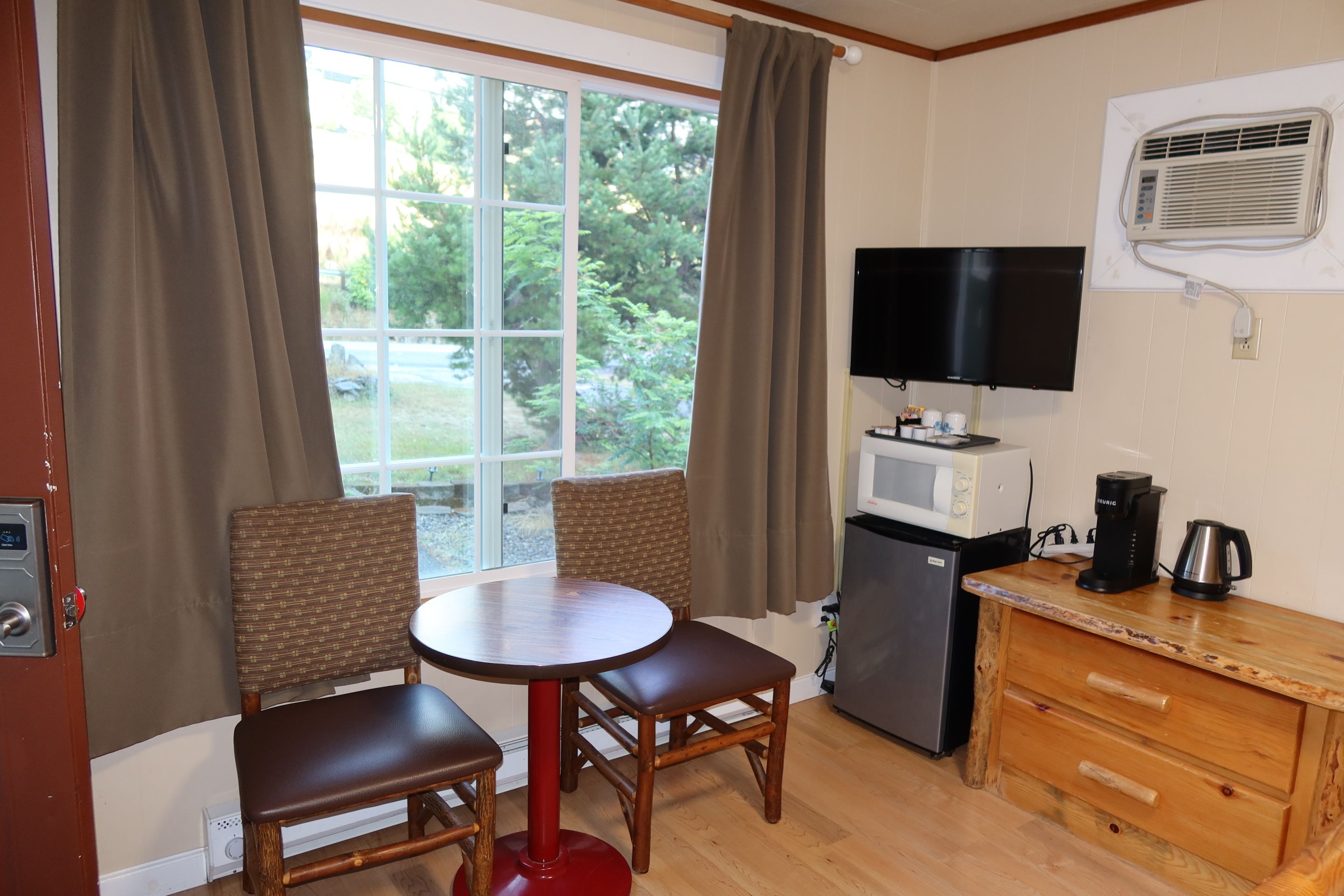 A compact room with a dining table, two chairs, a television, a refrigerator, and a coffee maker.