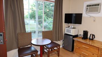 A compact room with a dining table, two chairs, a television, a refrigerator, and a coffee maker.