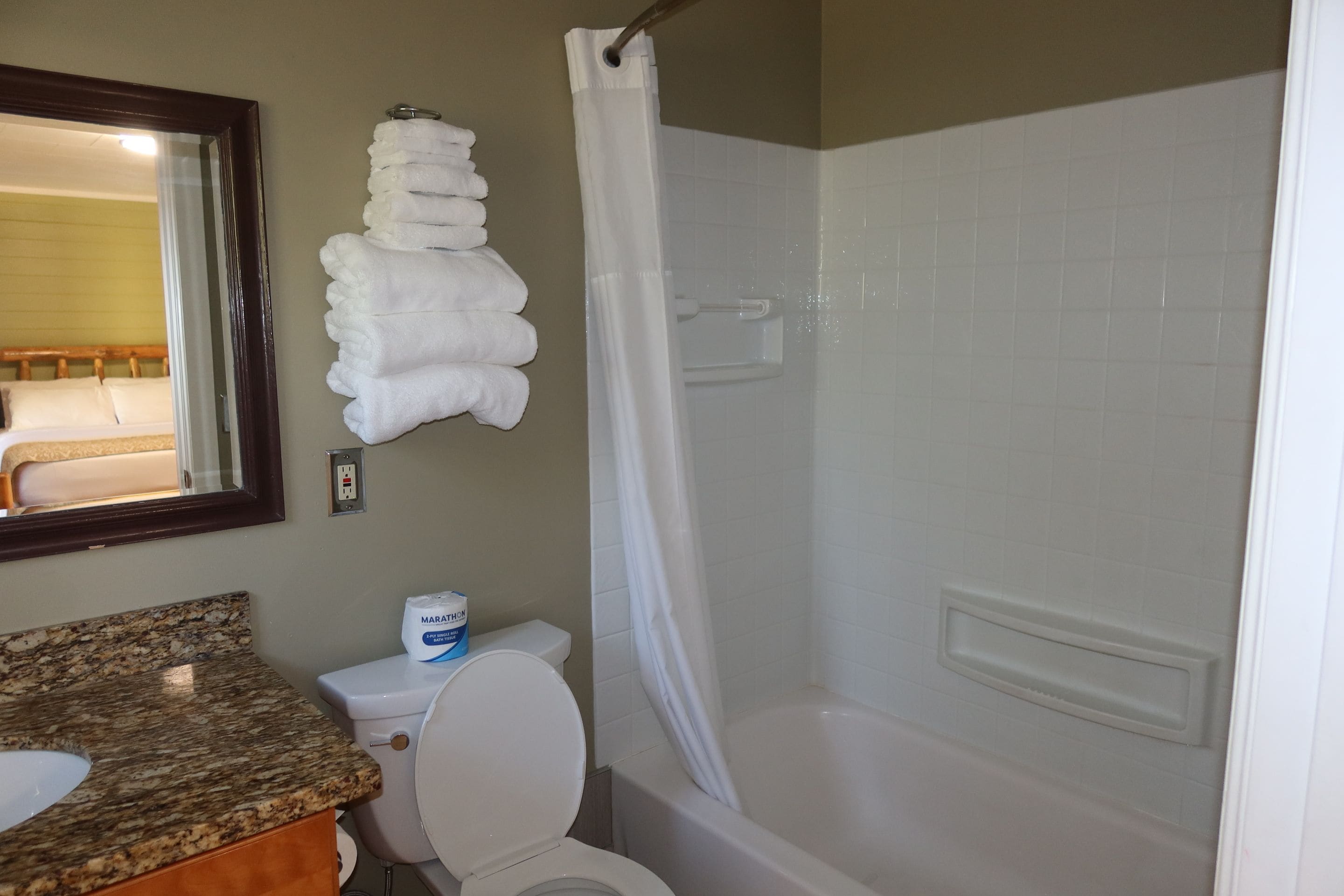 Un baño con inodoro, lavabo, ducha con cortina y un perchero con toallas dobladas.