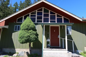 En grön byggnad med en röd dörr, en liten veranda och ett stort fönster.