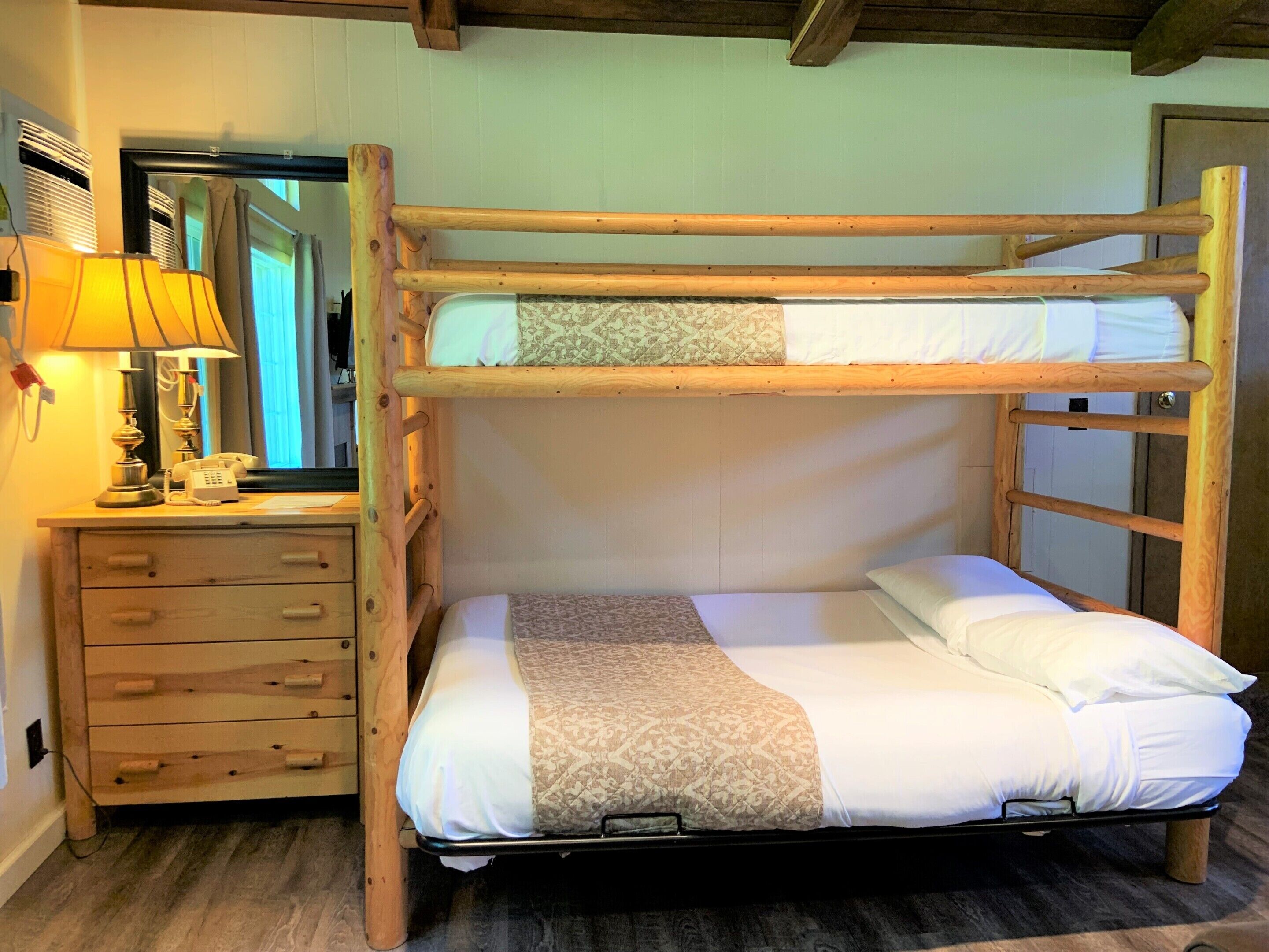 Una cama litera con estructura de madera, una mesita de noche con lámpara y un espejo.