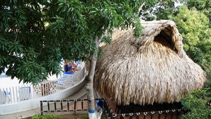 A thatched-roof hut with a white fence and a tree in the foreground. - Hostería Fundadores (Santa Fe de Antioquia)