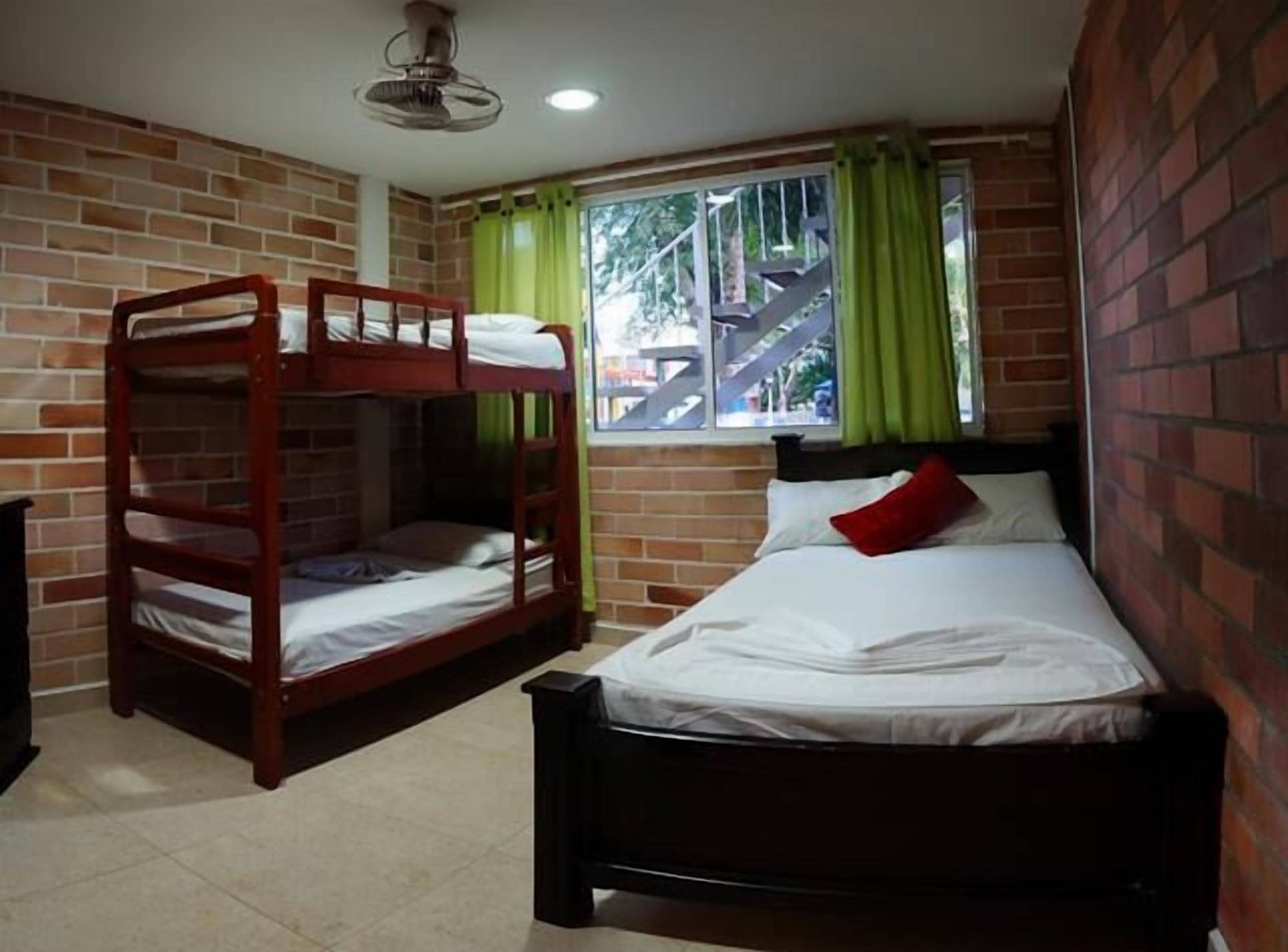 Una habitación con literas, una cama individual, un ventilador de techo y una ventana con cortinas.