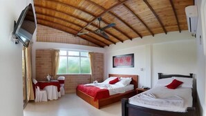 A bedroom with two beds, a TV mounted on the wall, and a large window. - Hostería Fundadores (Santa Fe de Antioquia)