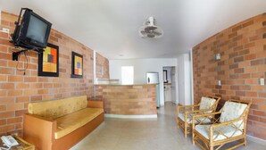 A living room with a brick wall, a sofa, two wicker chairs, a television, and a ceiling fan. - Hostería Fundadores (Santa Fe de Antioquia)