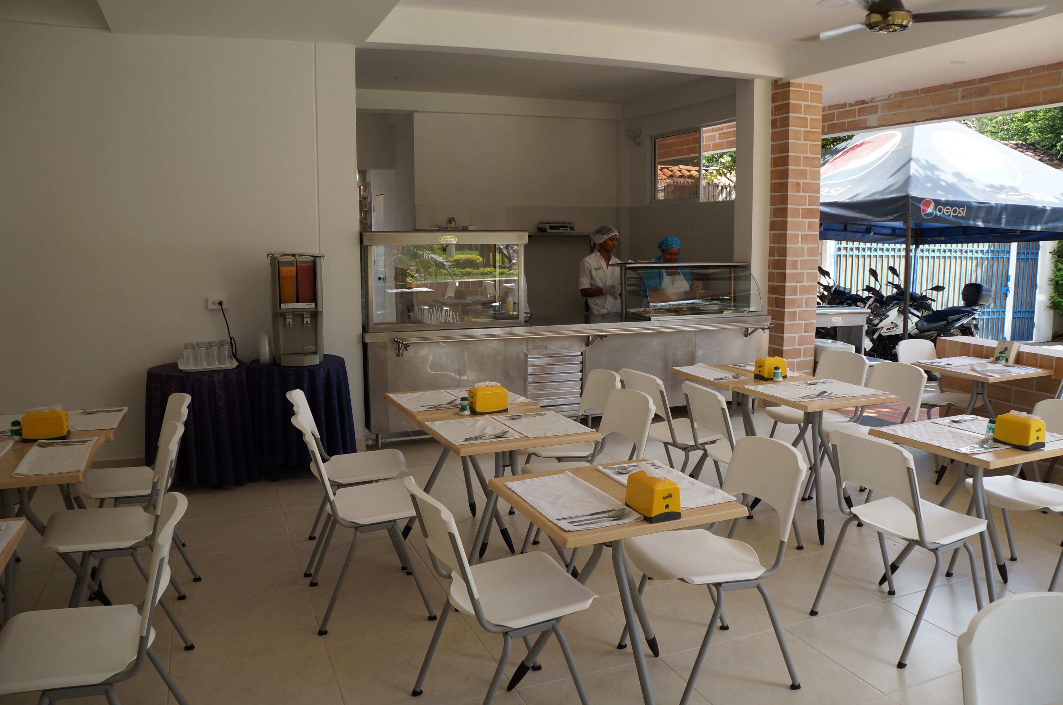 A classroom with tables and chairs, a water dispenser, and a refrigerator.
