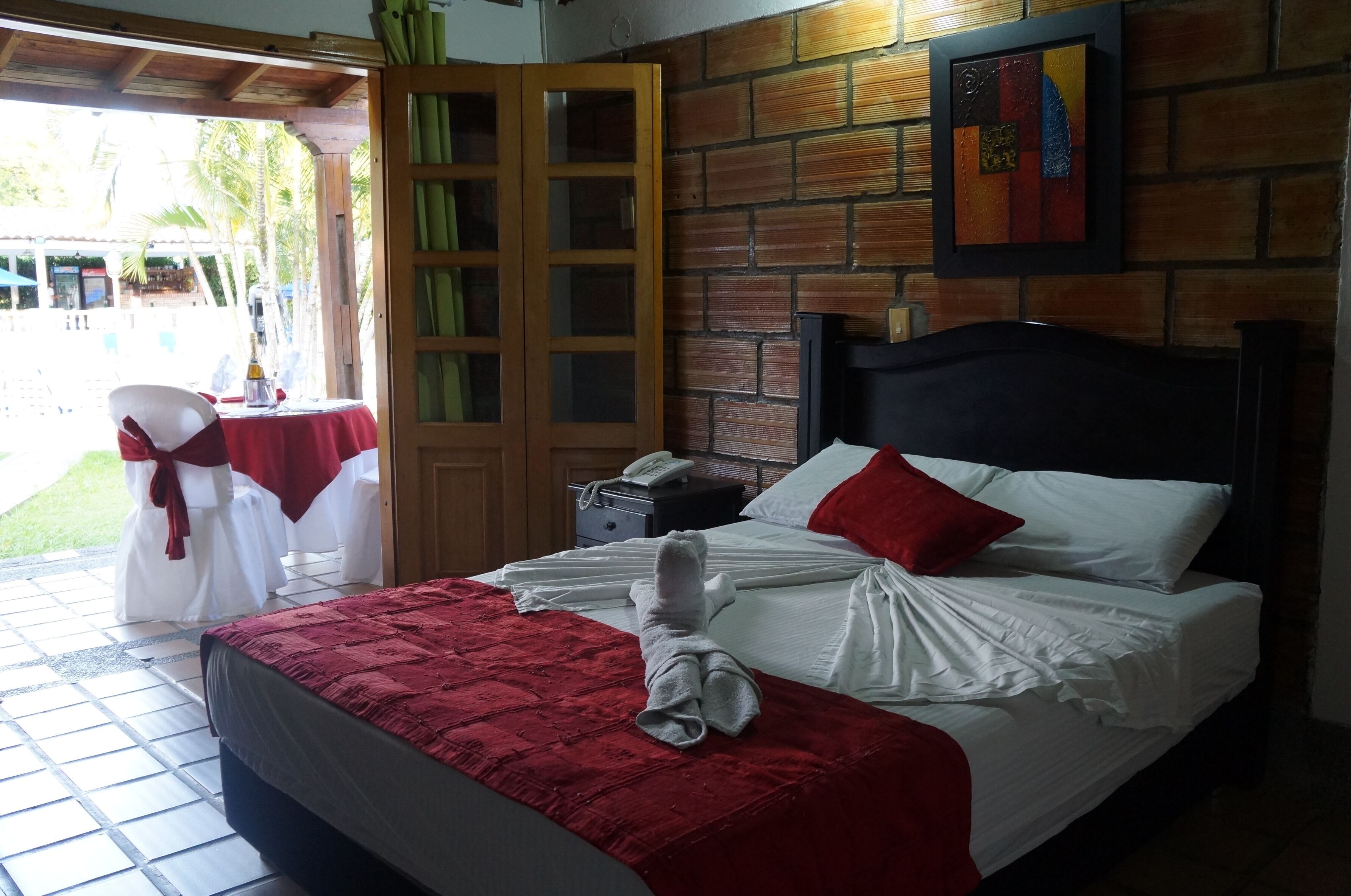 A hotel room with a bed, a nightstand, a wooden door, and a view of the outside.
