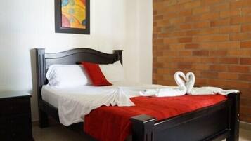 A bed with a red blanket and white sheets, a black headboard, and a red pillow.