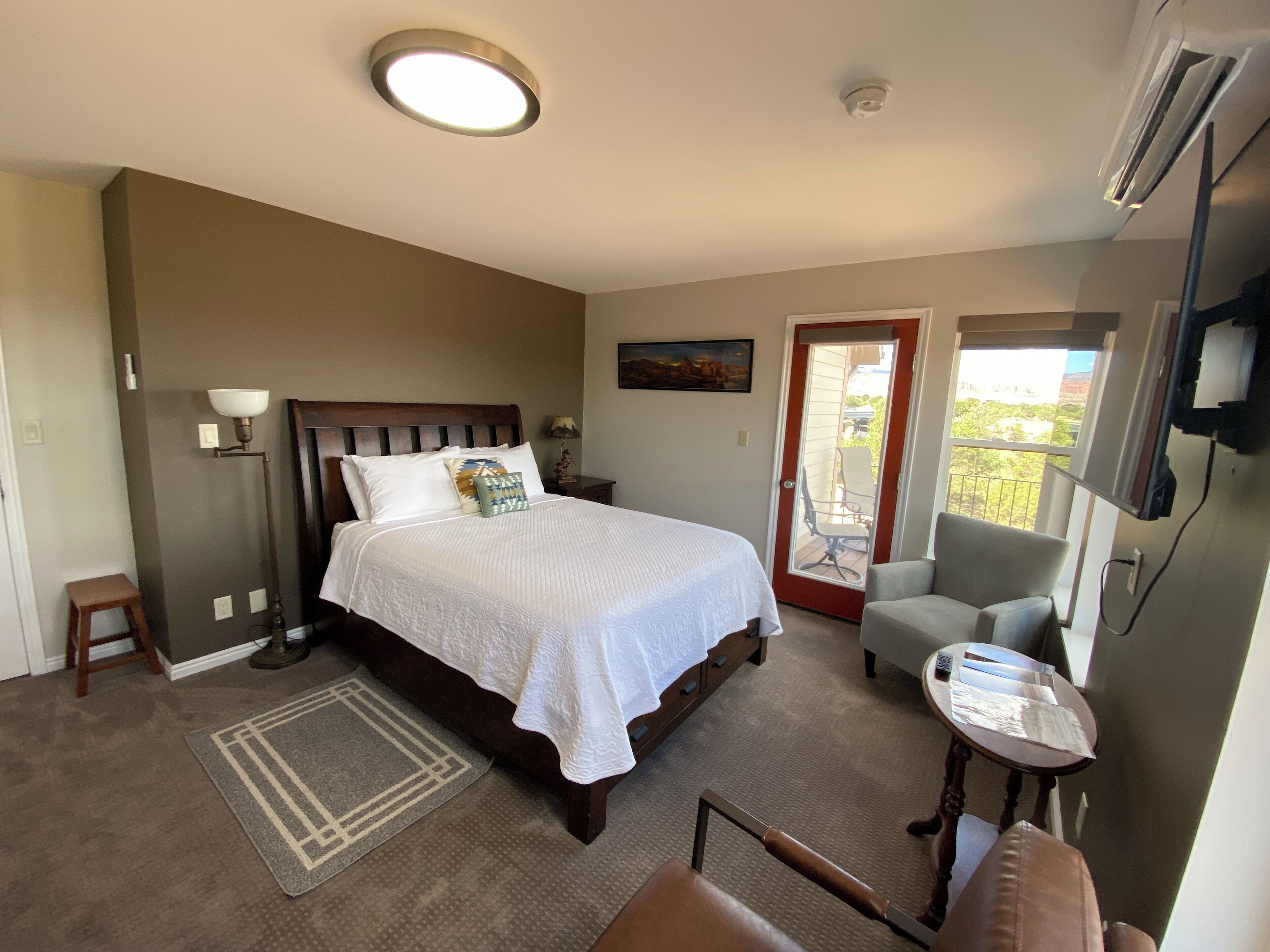 A bedroom with a bed, bedside table, lamp, chair, and a view through a door.