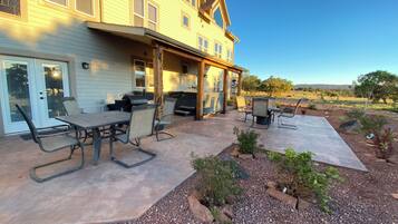 A two-story house with a patio area featuring a table and chairs, a grill, and a hot tub.