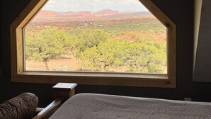 A room with a large window offering a view of a desert landscape with trees and distant buildings.