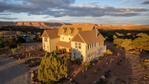 A large, two-story house with a prominent front porch, surrounded by a well-maintained garden and a clear view of the surrounding desert landscape.