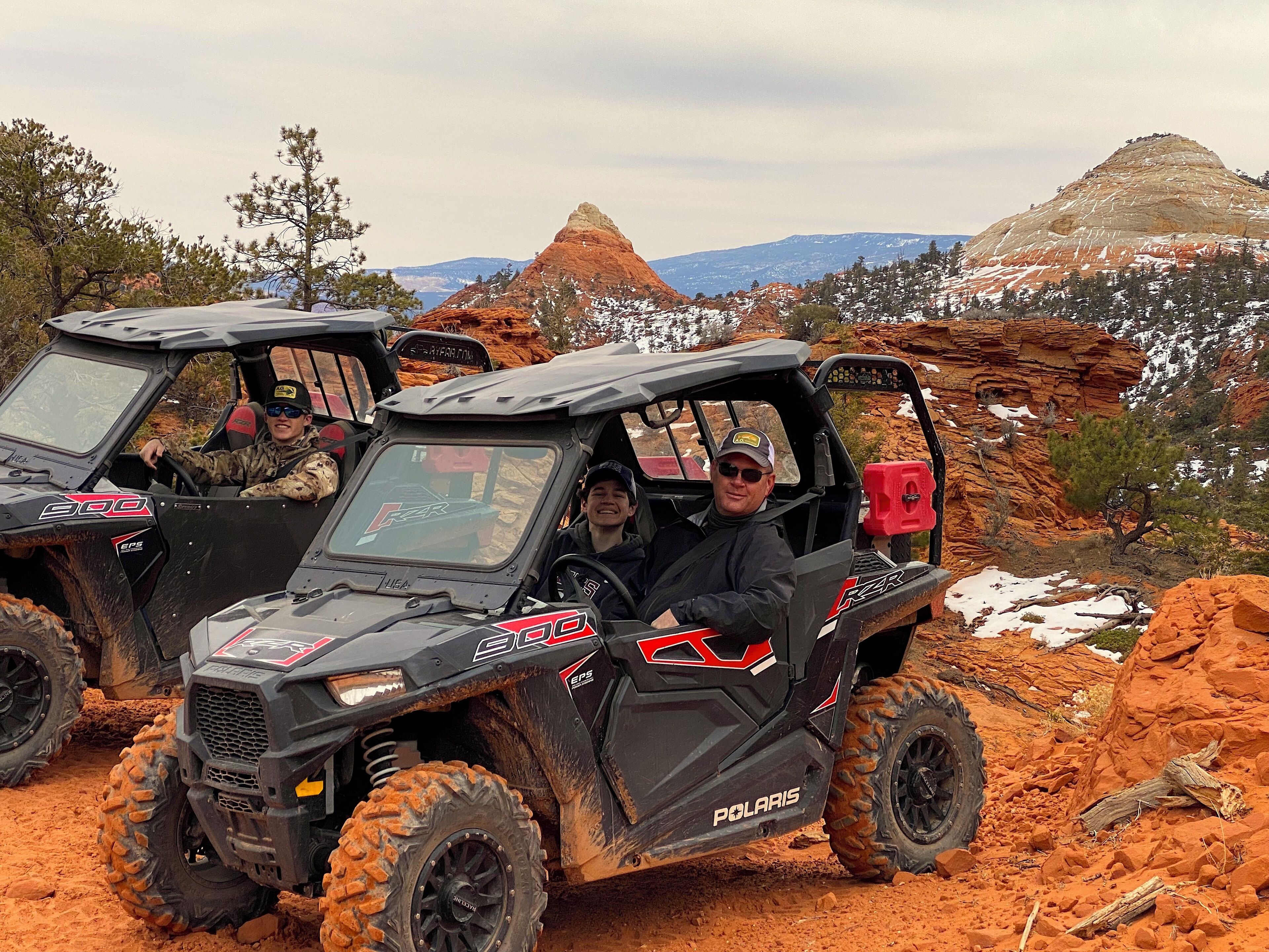 Deux véhicules Polaris 500 sont stationnés sur un chemin de terre, avec en arrière-plan un paysage montagneux et rocheux.