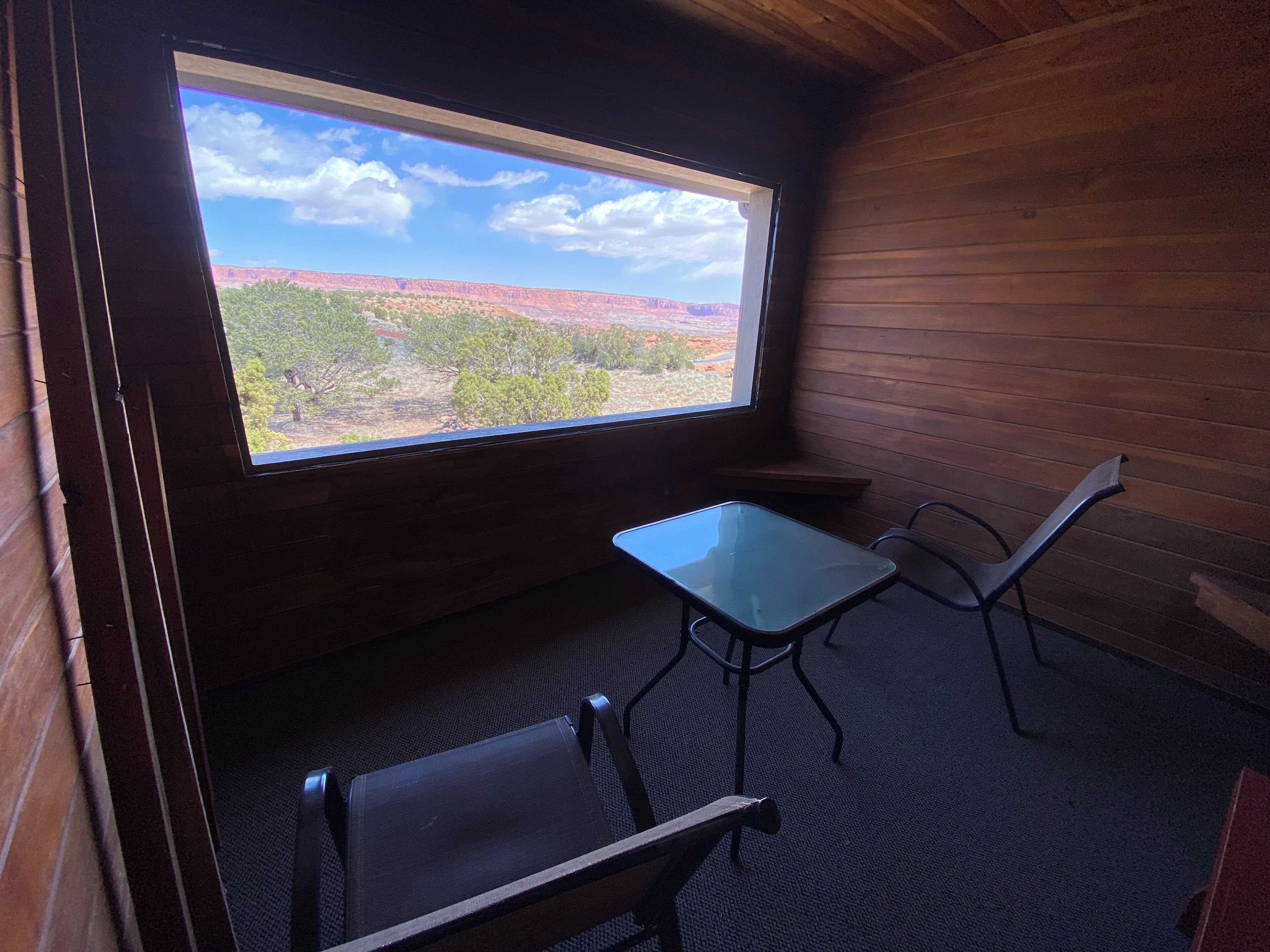 A room with a large window, a small table, two chairs, and a carpeted floor.