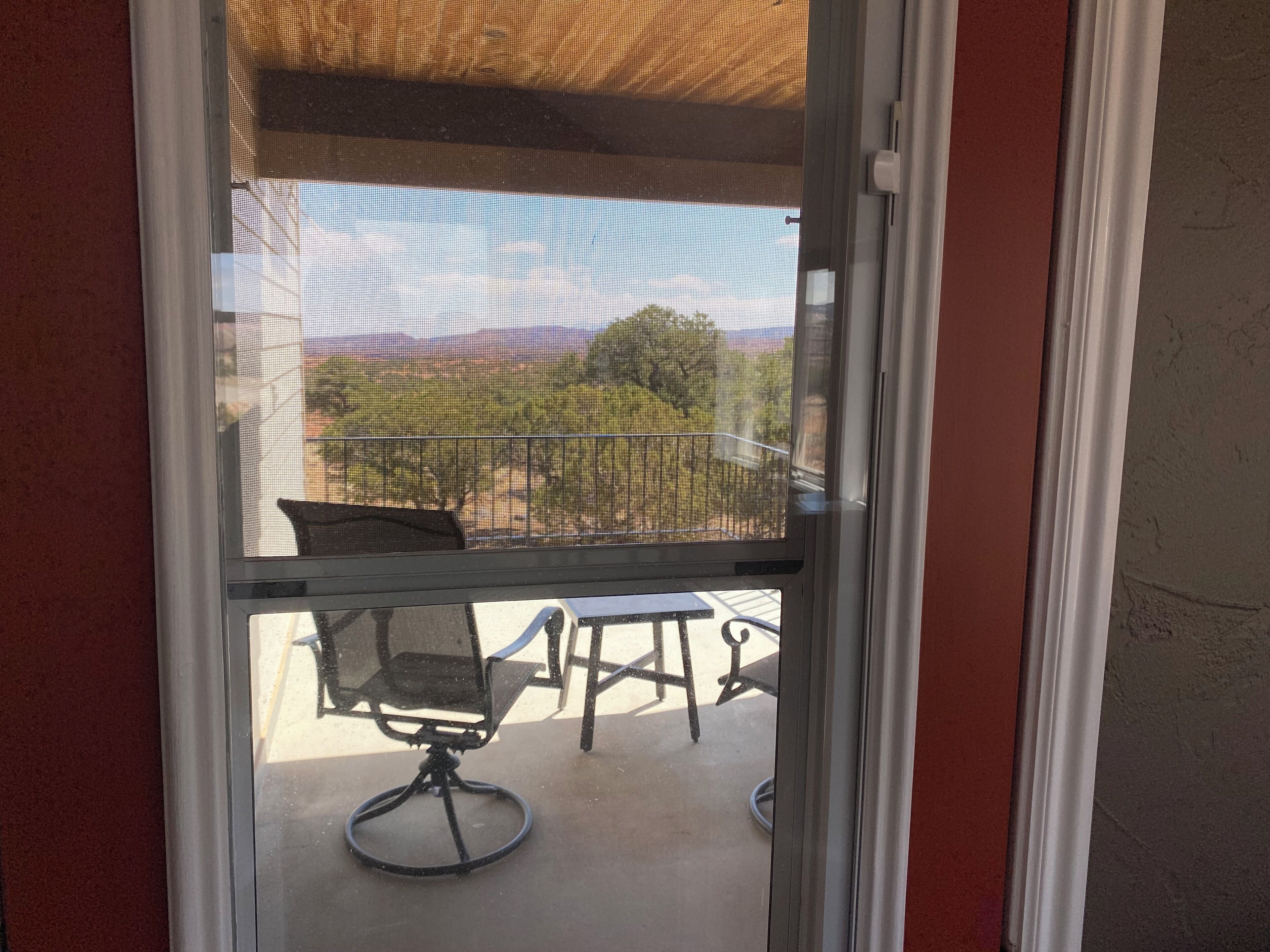 Blick durch ein Fenster mit einem Fliegengitter, ein Stuhl und ein Tisch auf einem Balkon.