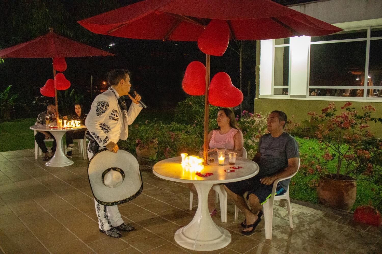 An outdoor patio area with round tables, red umbrellas, and heart-shaped decorations.