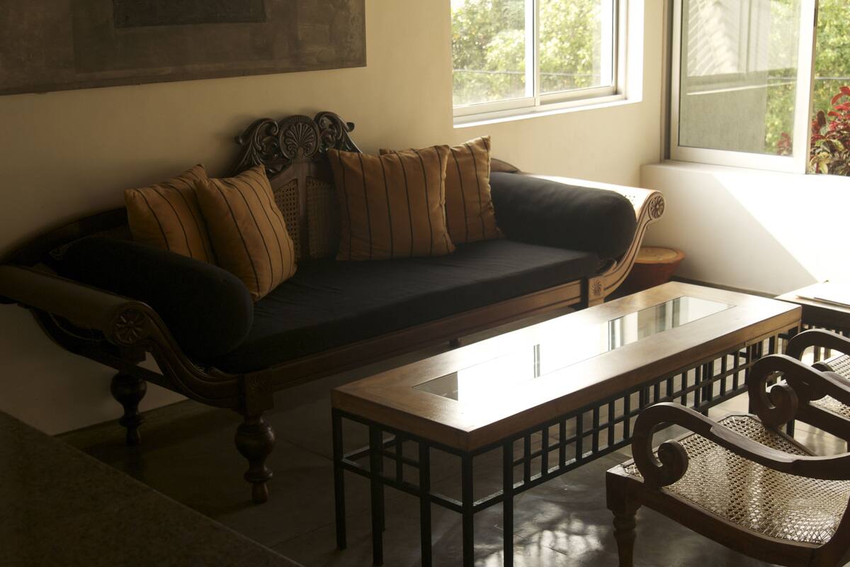 A dark-colored sofa with striped cushions, a wooden coffee table, and a wicker chair in a room with a large window.