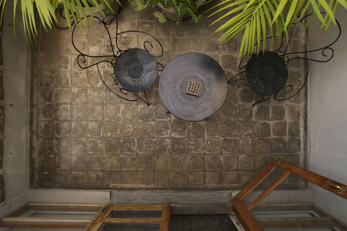 A room with a tiled wall, a metal-framed shelf with decorative plates, and a wooden chair.