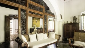 A room with a large ornate mirror, a wooden sofa, a wicker chair, and a wooden cabinet. - Nisala Arana Boutique Hotel (Bentota)
