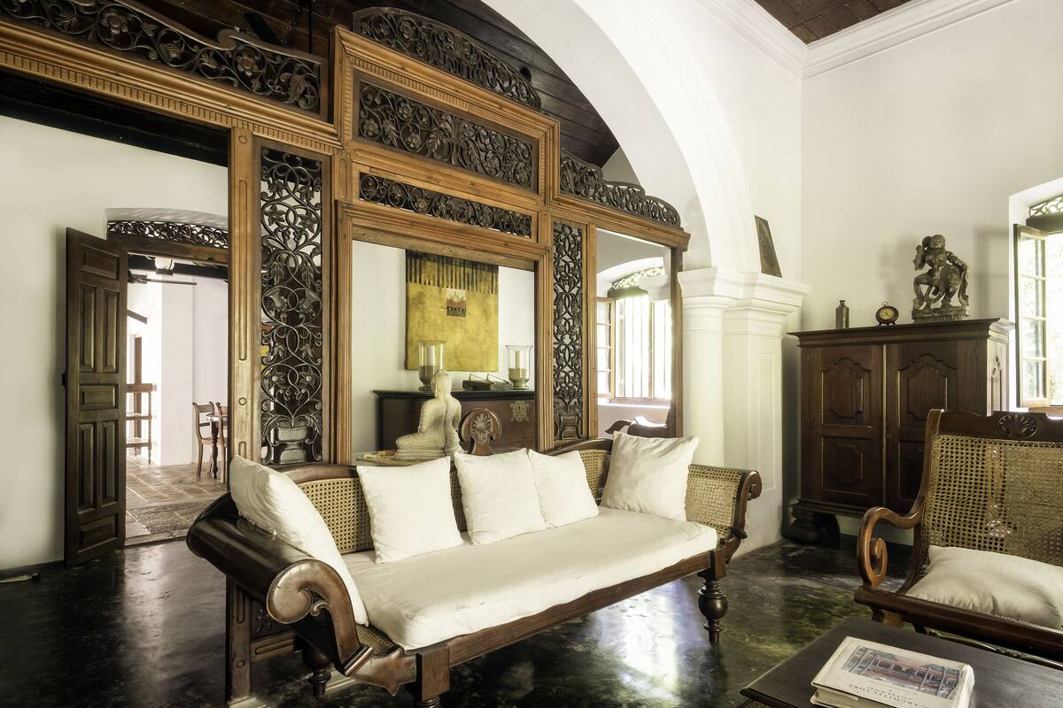 Une pièce comprenant un grand miroir décoratif, un canapé en bois, une chaise en osier et un meuble en bois.