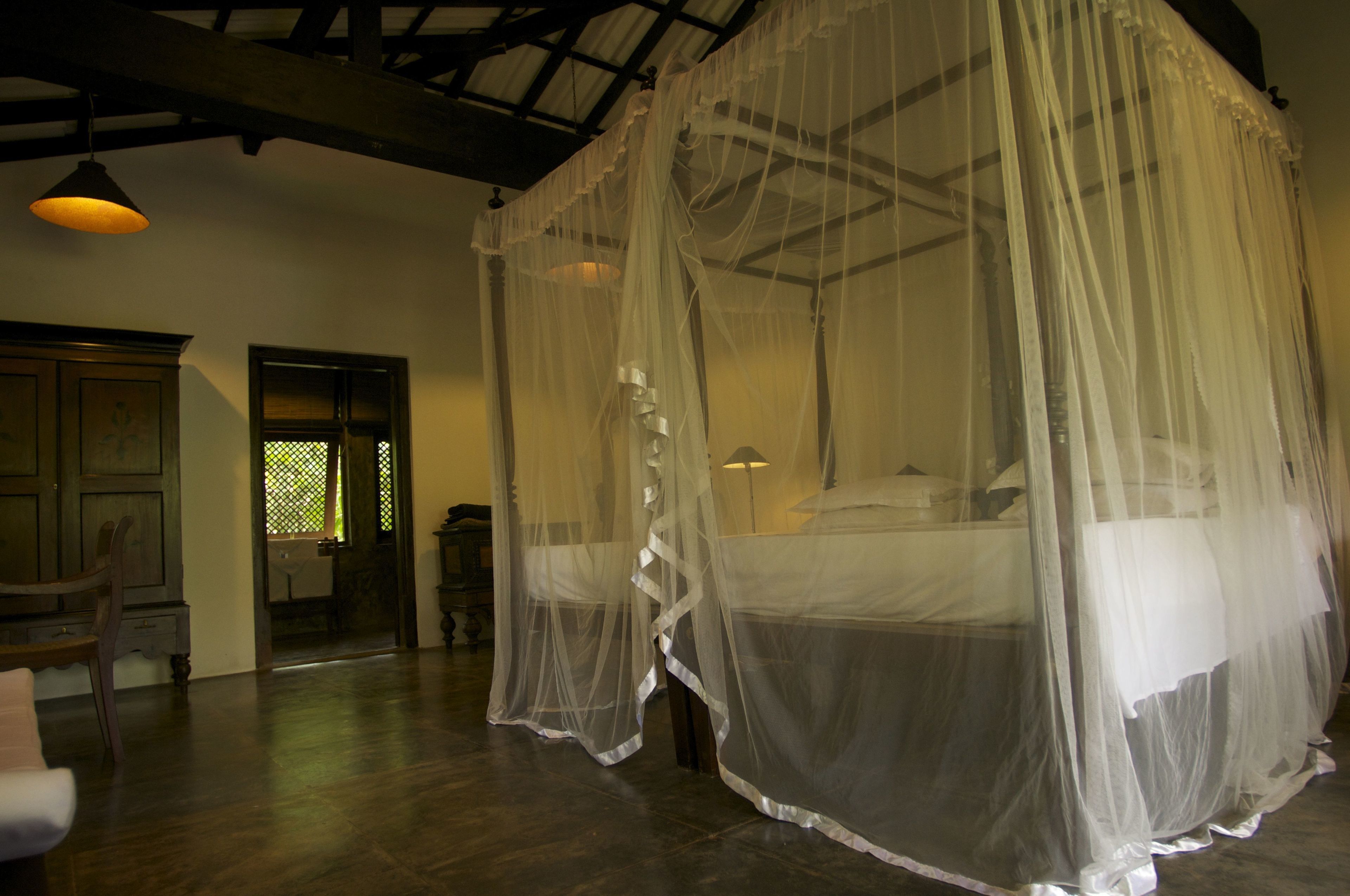 A room with a four-poster bed covered by a sheer canopy, wooden flooring, and a traditional wooden door.