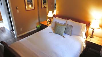 A neatly made bed with white linens, two bedside lamps, and a green trash bin.