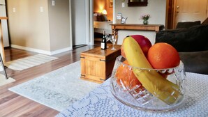 A living room with a wooden coffee table, a glass fruit bowl with apples, oranges, and bananas, and a couch. - Belle Neige Suites- Whistler (Whistler)