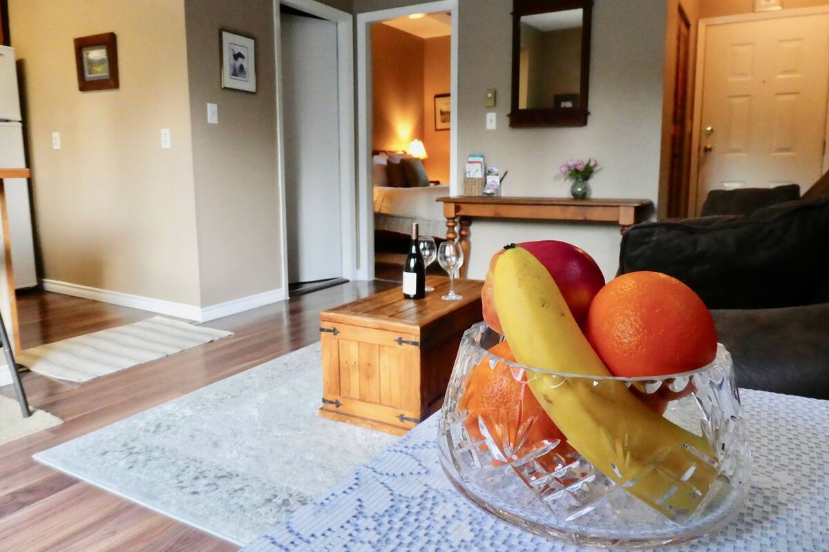 A living room with a wooden coffee table, a glass fruit bowl with apples, oranges, and bananas, and a couch.