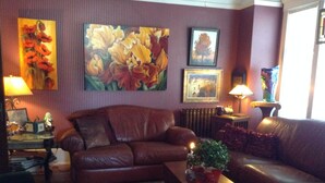 Ein Wohnzimmer mit einem braunen Ledersofa, einem Couchtisch mit einer Pflanze und einem Kamin. Auf Nachttischen stehen zwei Lampen und an der Wand hängt ein gerahmtes Bild.