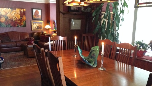 Ein Essbereich mit einem Holztisch, Stühlen und einer Vase mit Kerzen. Im Hintergrund befindet sich eine Couch und eine Pflanze.