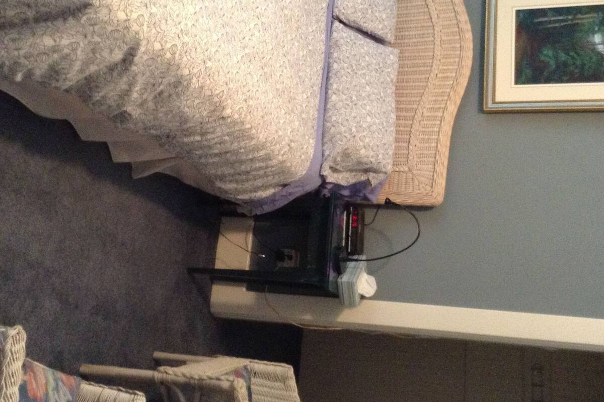A bedroom with a bed, a bedside table, a lamp, a framed picture on the wall, and a chair.