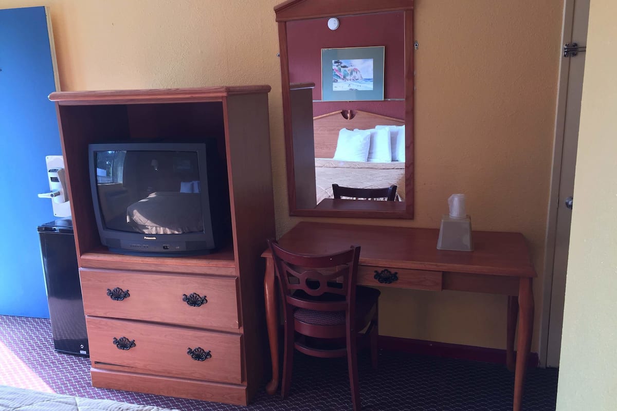 A wooden desk with a television, a chair, and a mirror.