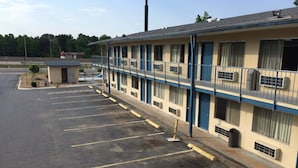 A motel with a row of rooms, a parking lot, and a small building with a sign. - Super 7 Inn (Little Rock)