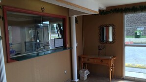 A reception area with a glass counter, a wooden desk, and a mirror on the wall. - Super 7 Inn (Little Rock)