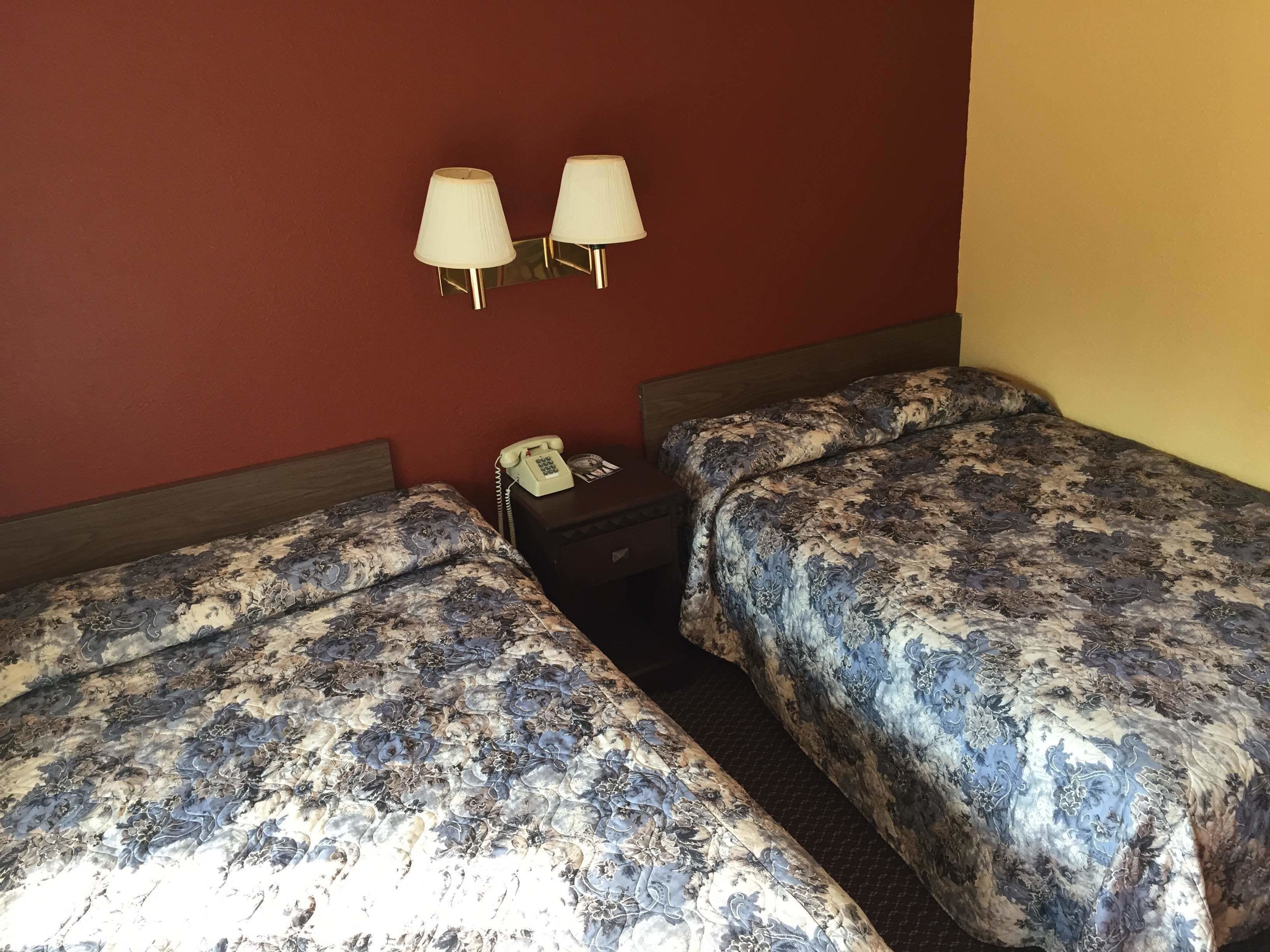 A hotel room with two beds, a nightstand with a telephone, and wall-mounted lamps.