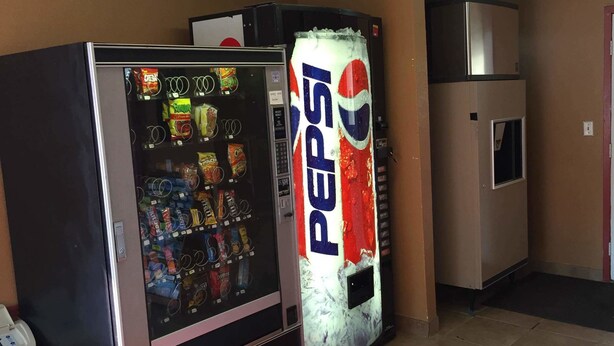 A vending machine stocked with snacks and a large Pepsi refrigerator. - Super 7 Inn (Little Rock)