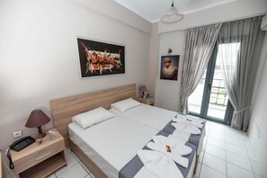 Habitación de hotel con una cama grande, una mesita de noche con lámpara, un cuadro en la pared y una ventana con cortinas.