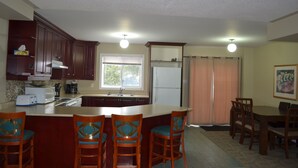 A kitchen with wooden cabinets, a central island with bar stools, a refrigerator, and a dining area with chairs and a table. - Downtown Whitby Furnished Homes (Whitby)