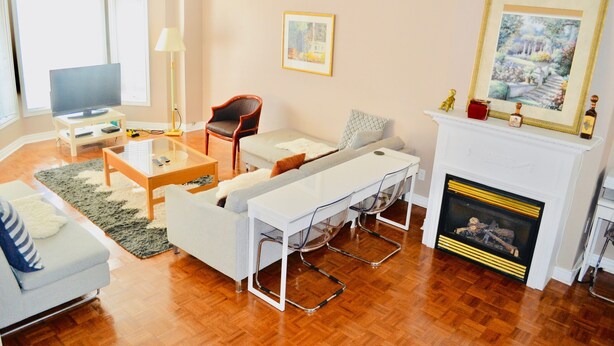 A living room with a sofa, a coffee table, a TV, a fireplace, and a painting on the wall. - Downtown Whitby Furnished Homes (Whitby)
