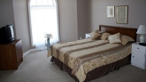 A bedroom with a large bed, a nightstand, a dresser, a television, and a window with curtains. - Downtown Whitby Furnished Homes (Whitby)