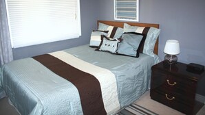 A neatly made bed with a striped bedspread, a bedside table with a lamp, and a framed picture on the wall. - Downtown Whitby Furnished Homes (Whitby)