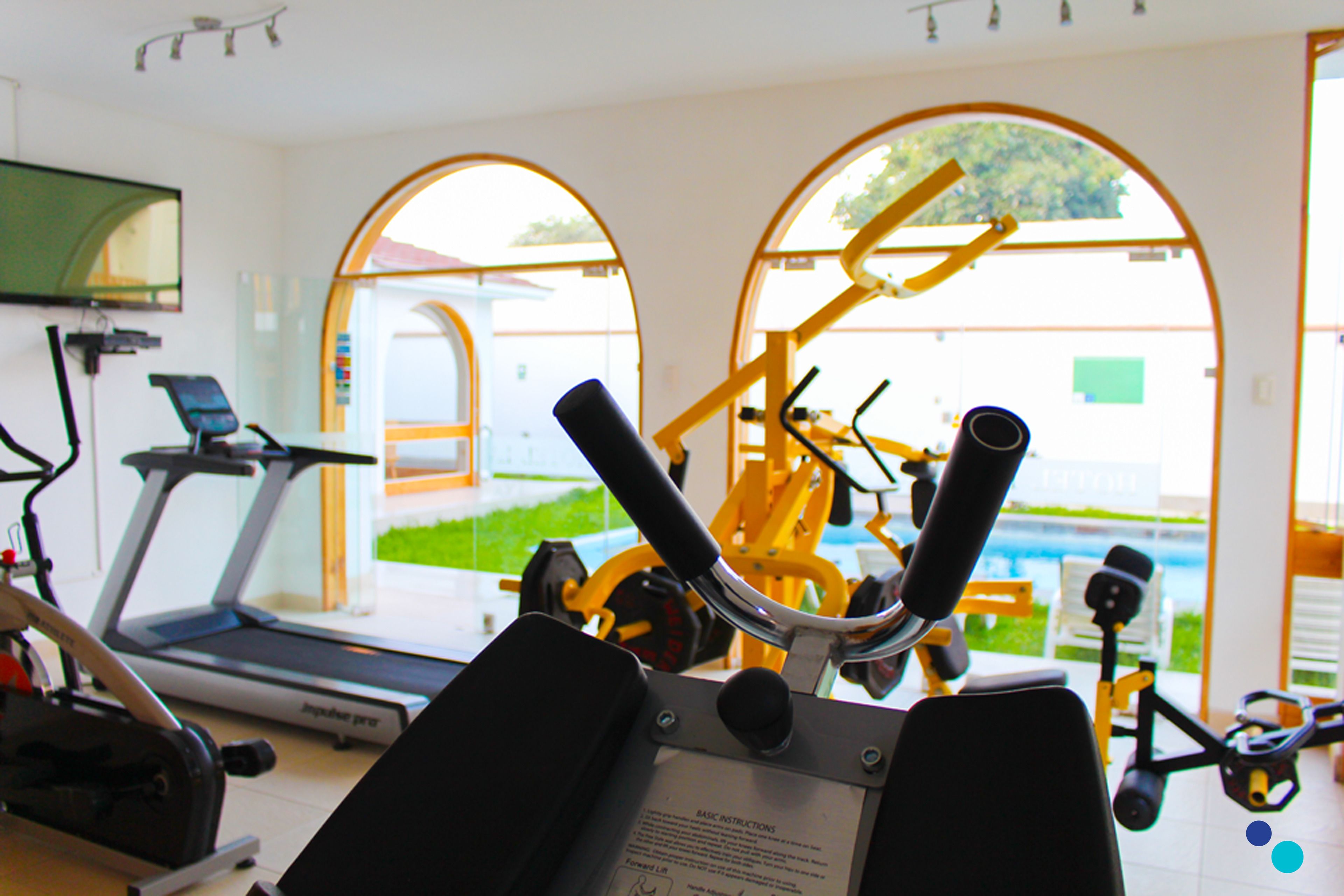 Une salle de sport équipée de matériel d’exercice, d’un tapis de course et de grandes fenêtres donnant sur l’extérieur.