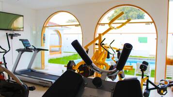 Un gimnasio con equipo de ejercicio, una cinta de correr y amplios ventanales que dan al exterior.