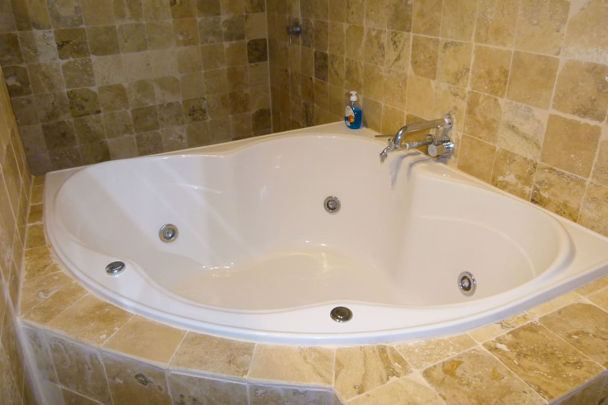 A large, white freestanding bathtub with a single faucet and drain, set against a tiled wall with a beige and brown pattern.