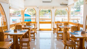 A restaurant with wooden tables and chairs, large windows, and an air conditioning unit.