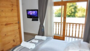 A hotel room with a bed, a television mounted on the wall, and a balcony with a wooden railing.