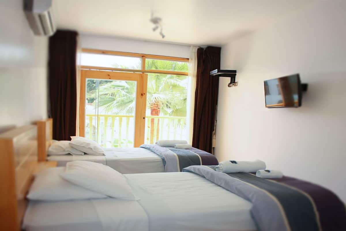 A hotel room with two beds, a large window with curtains, a mounted TV, and a ceiling fan.