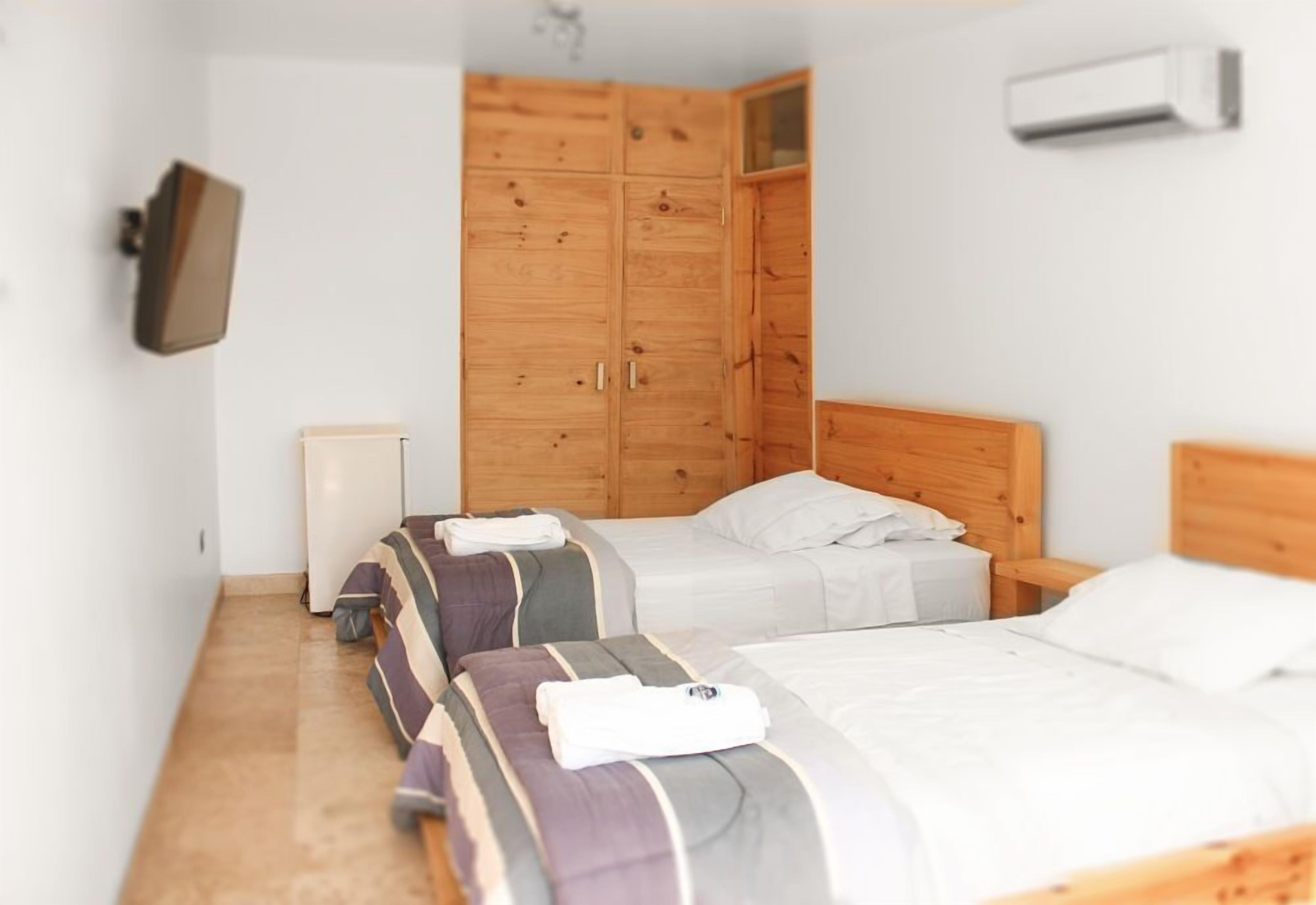 Quarto de hotel com duas camas, um guarda-roupa de madeira, uma televisão de tela plana e um aparelho de ar condicionado.