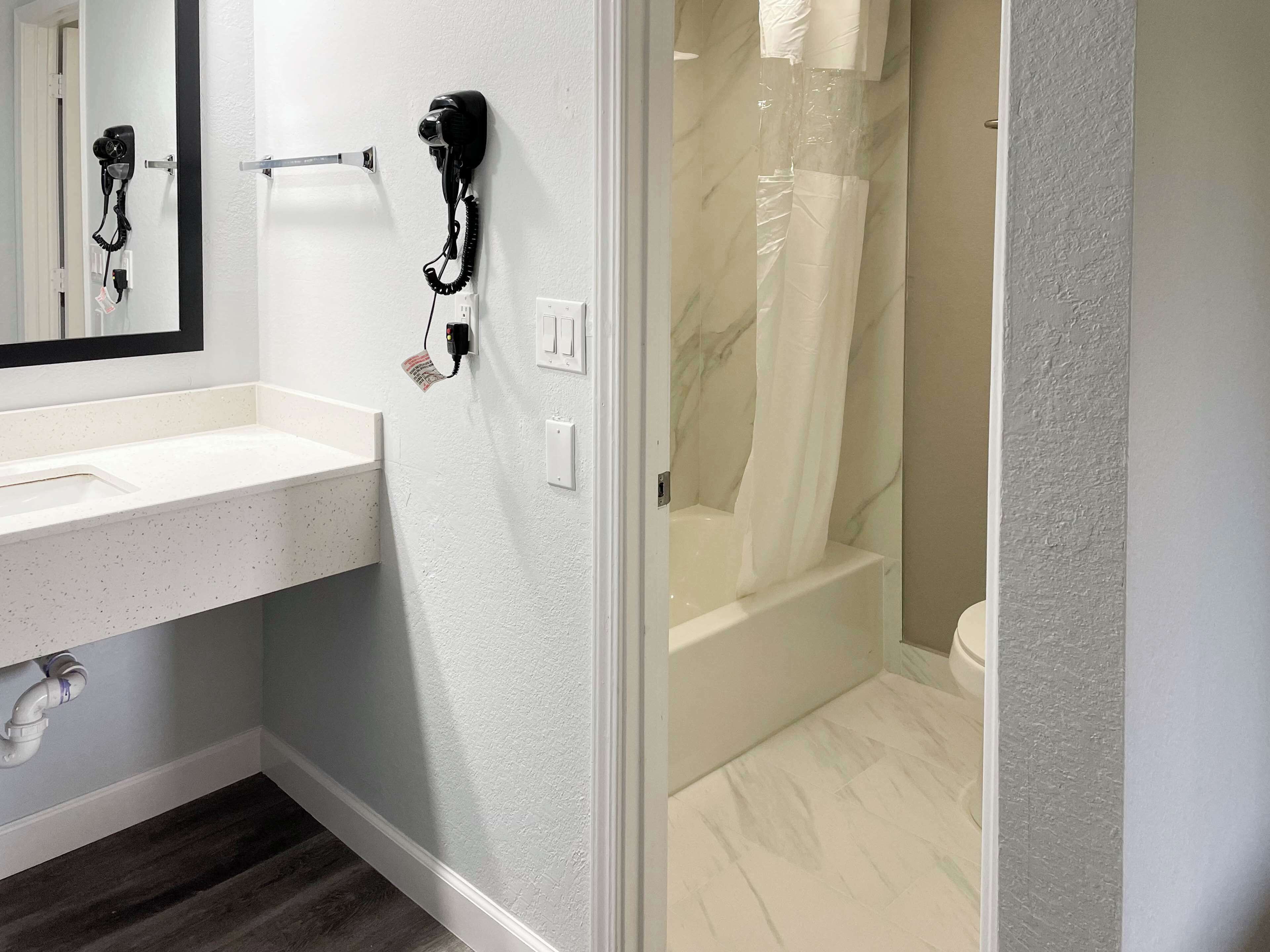 A bathroom with a white sink, a hairdryer mounted on the wall, and a glass-enclosed shower area.