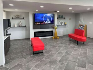 A modern living room with a flat-screen TV, red seating, a coffee machine, and decorative vases.